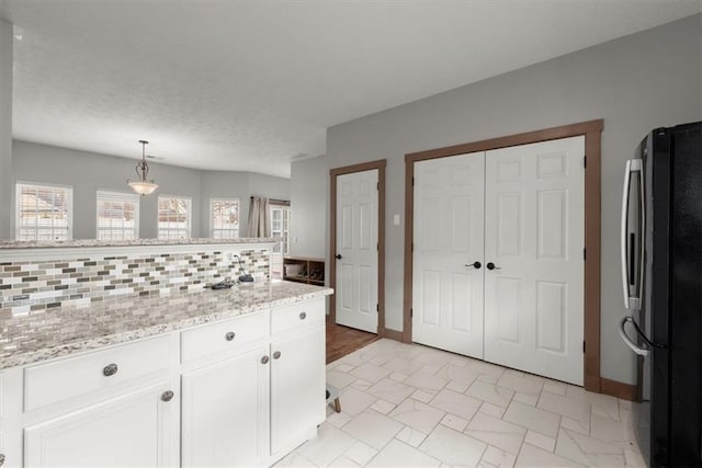 kitchen with white cabinets, decorative backsplash, decorative light fixtures, light stone counters, and stainless steel refrigerator