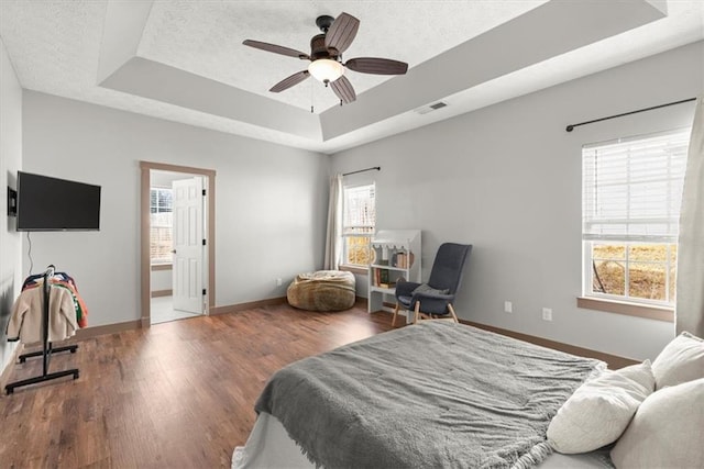 bedroom featuring multiple windows, connected bathroom, a tray ceiling, and ceiling fan