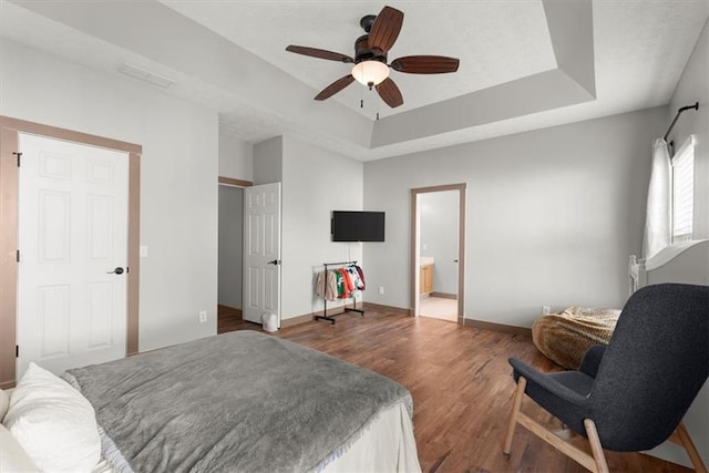 bedroom with a raised ceiling, connected bathroom, ceiling fan, and dark hardwood / wood-style flooring