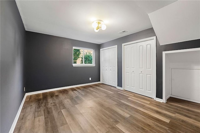 unfurnished bedroom with hardwood / wood-style floors and multiple closets