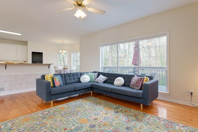 living room with baseboards, ceiling fan with notable chandelier, and light wood finished floors