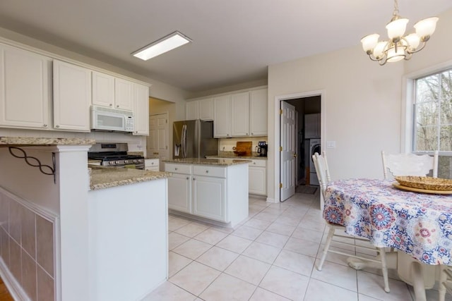 kitchen with light tile patterned floors, light stone counters, washer / dryer, white cabinets, and appliances with stainless steel finishes