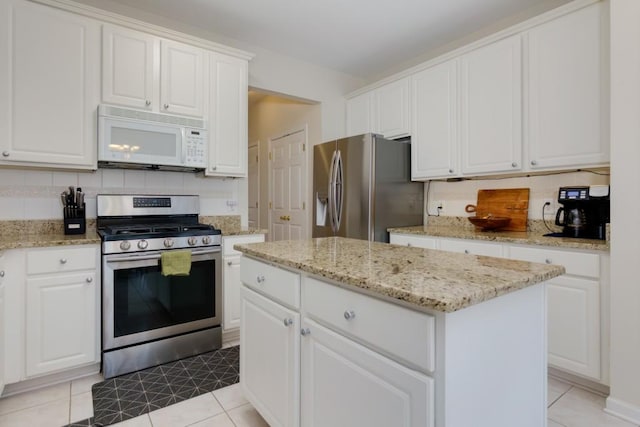 kitchen featuring light stone countertops, a kitchen island, stainless steel appliances, decorative backsplash, and white cabinets