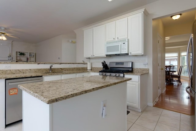 kitchen with light tile patterned floors, a kitchen island, a sink, white cabinets, and appliances with stainless steel finishes