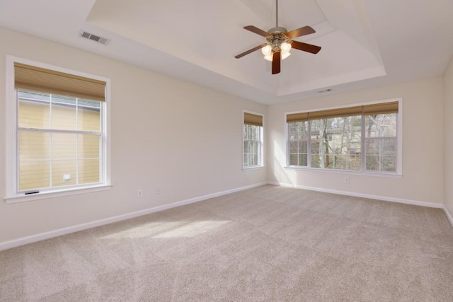 carpeted spare room with a tray ceiling, baseboards, and visible vents