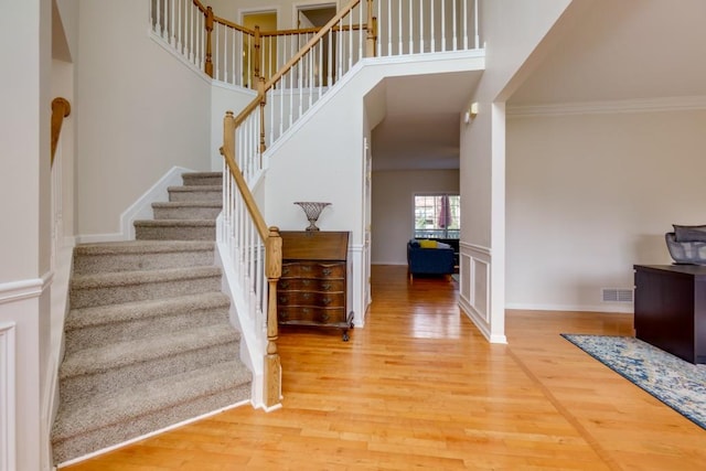 stairway featuring visible vents, crown molding, a towering ceiling, and wood finished floors