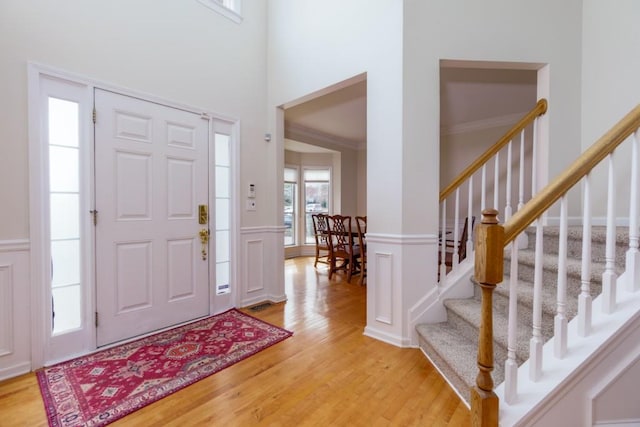 entrance foyer featuring crown molding, stairway, wainscoting, light wood-style floors, and a decorative wall