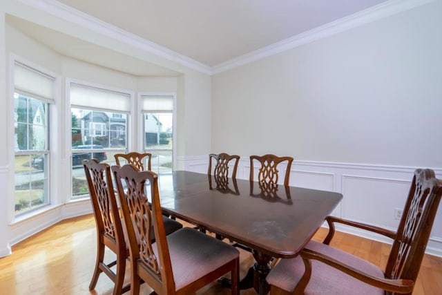 dining space featuring a wainscoted wall, a decorative wall, light wood-style floors, and ornamental molding