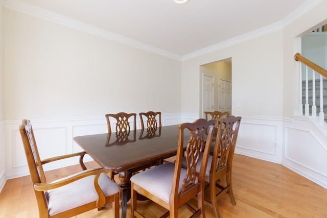 dining room with wainscoting, crown molding, stairs, and light wood-type flooring