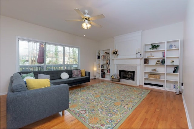 living area featuring ceiling fan, light wood-type flooring, baseboards, and a fireplace with raised hearth