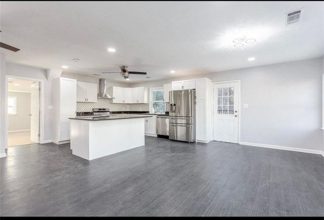 kitchen with wall chimney range hood, a kitchen island, ceiling fan, stainless steel appliances, and white cabinets