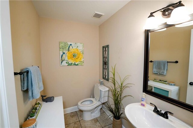 half bath with a sink, toilet, tile patterned flooring, and baseboards