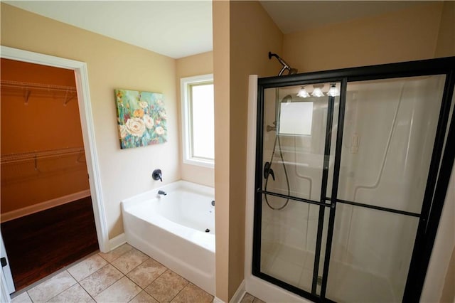 bathroom with a stall shower, a garden tub, a walk in closet, tile patterned floors, and baseboards