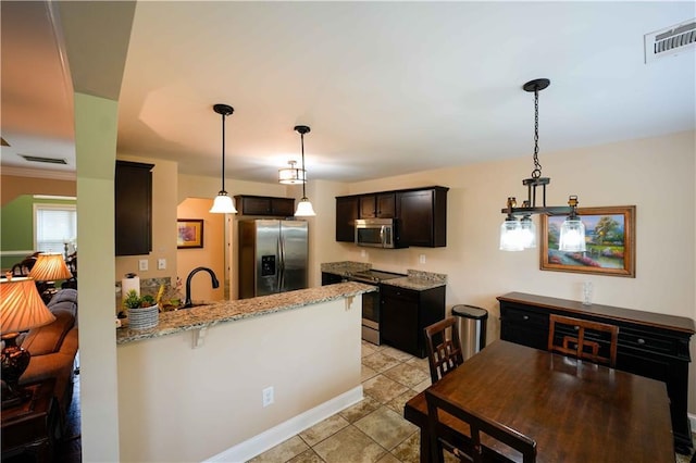 kitchen with appliances with stainless steel finishes, a peninsula, light stone counters, and decorative light fixtures