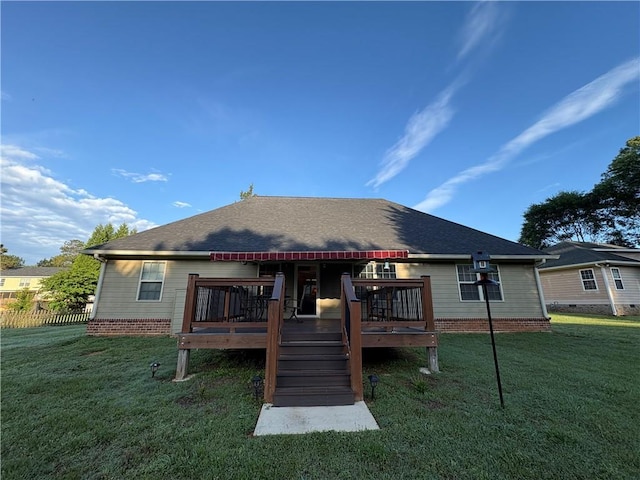 rear view of property featuring a wooden deck, a lawn, and a shingled roof