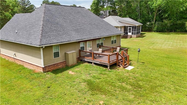 rear view of property featuring a sunroom, roof with shingles, a wooden deck, and a lawn