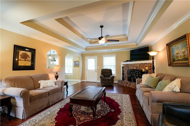 living room with a raised ceiling, crown molding, a ceiling fan, a fireplace, and wood finished floors