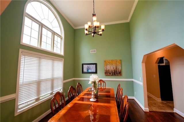dining area featuring a chandelier, a towering ceiling, wood finished floors, crown molding, and baseboards