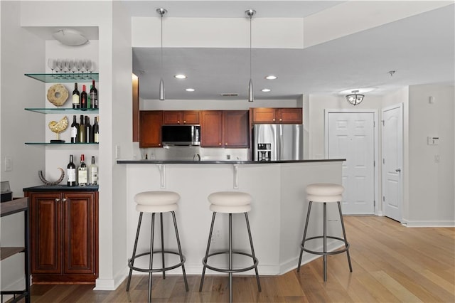 kitchen with a kitchen breakfast bar, dark countertops, appliances with stainless steel finishes, and light wood-style flooring