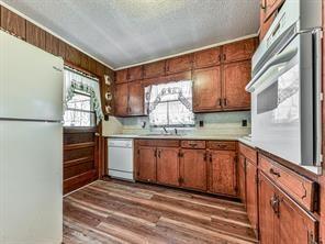 6267 Mount Pisgah Rd, Ellijay, GA 30540 - kitchen with a textured ceiling, wood finished floors, white appliances, brown cabinetry, and light countertops