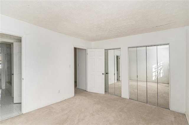 unfurnished bedroom with light carpet, a textured ceiling, connected bathroom, and multiple closets