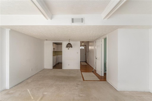 empty room with light carpet, beamed ceiling, a textured ceiling, and visible vents