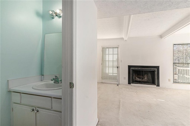 bathroom featuring beamed ceiling, a fireplace, a textured ceiling, and vanity