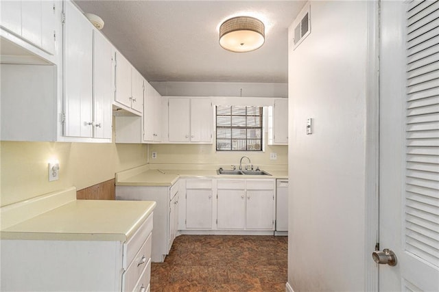 kitchen featuring visible vents, white dishwasher, light countertops, white cabinetry, and a sink