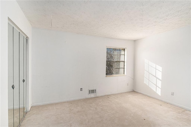 empty room with baseboards, a textured ceiling, visible vents, and carpet flooring