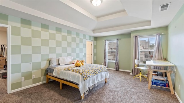 carpeted bedroom featuring an accent wall, a tray ceiling, and baseboards