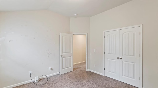 unfurnished bedroom with lofted ceiling, a closet, carpet flooring, and baseboards