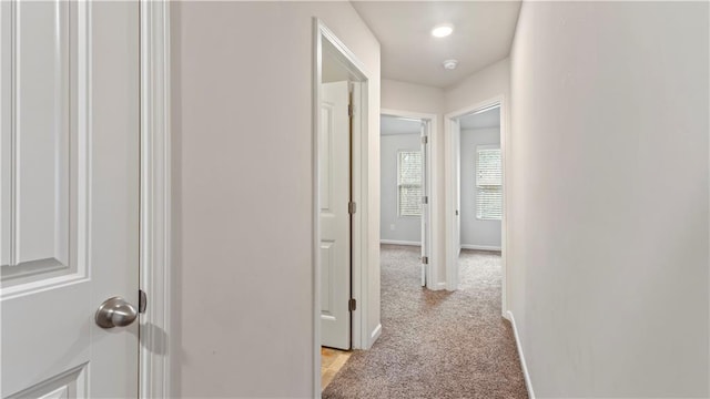 corridor featuring light colored carpet and baseboards