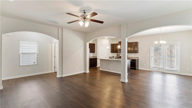 unfurnished living room with ceiling fan with notable chandelier, dark wood-style flooring, visible vents, and a healthy amount of sunlight