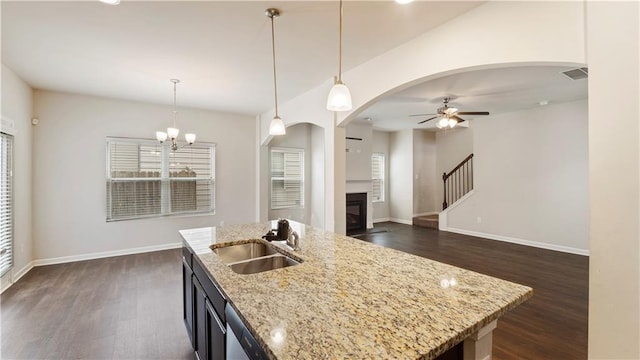 kitchen with a glass covered fireplace, dark wood-type flooring, pendant lighting, a sink, and ceiling fan with notable chandelier