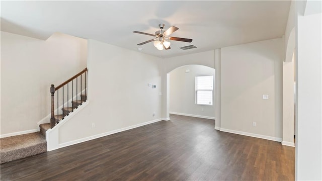 spare room with baseboards, dark wood finished floors, arched walkways, ceiling fan, and stairway