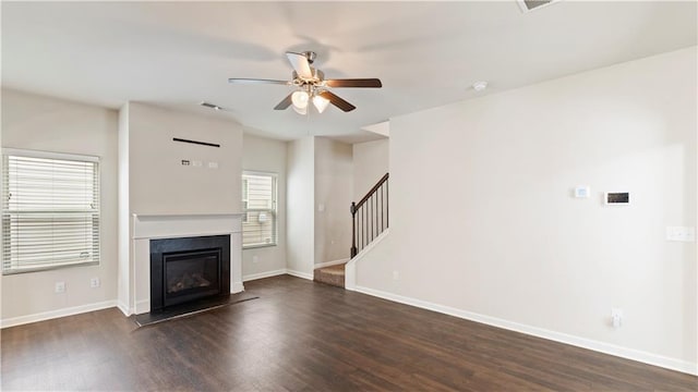 unfurnished living room with a glass covered fireplace, dark wood-style flooring, baseboards, and stairs