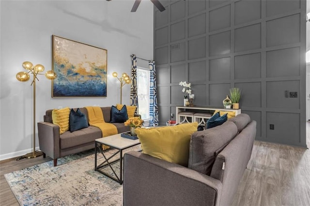 living room with ceiling fan, a decorative wall, a high ceiling, wood finished floors, and baseboards