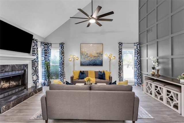 living area with visible vents, ceiling fan, wood finished floors, a fireplace, and a decorative wall