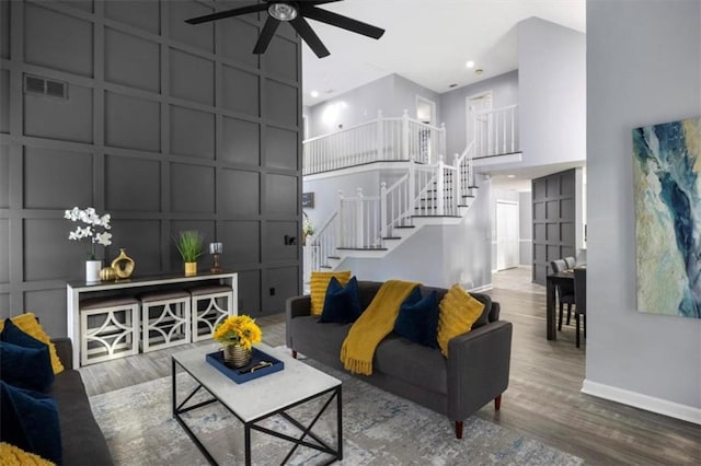 living room featuring a high ceiling, stairway, wood finished floors, and a decorative wall