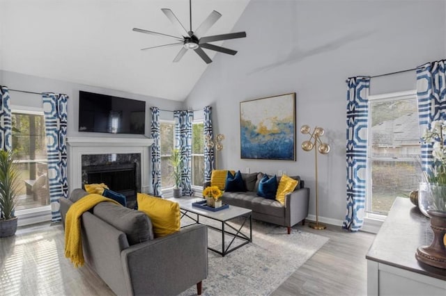 living area with light wood finished floors, baseboards, ceiling fan, a premium fireplace, and high vaulted ceiling