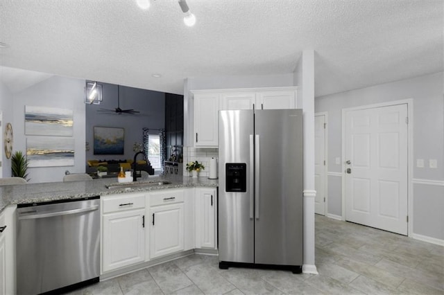 kitchen with light stone counters, appliances with stainless steel finishes, a ceiling fan, white cabinets, and a sink