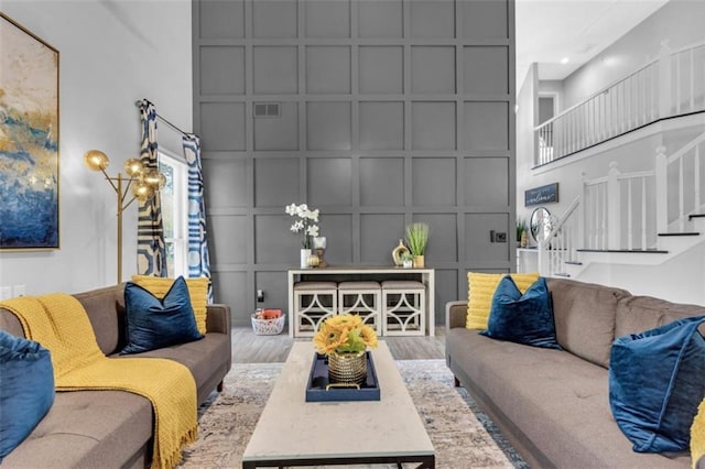 living area featuring visible vents, a decorative wall, a high ceiling, wood finished floors, and stairs