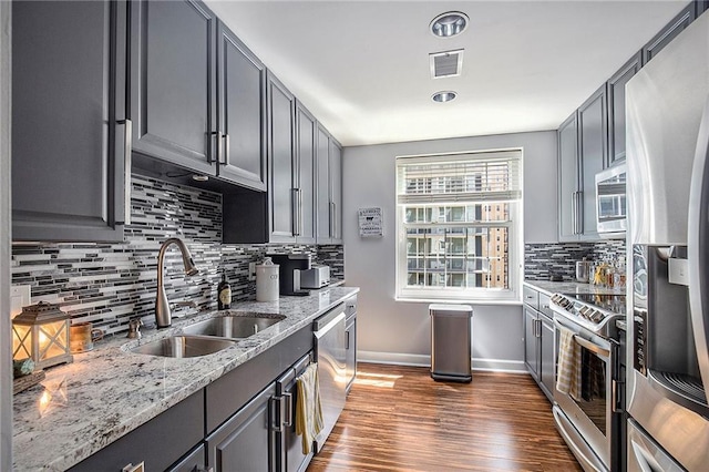 kitchen with appliances with stainless steel finishes, sink, gray cabinetry, dark hardwood / wood-style flooring, and light stone counters