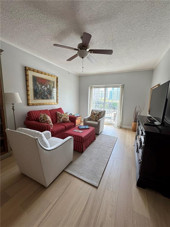 living room with hardwood / wood-style flooring, ornamental molding, ceiling fan, and a textured ceiling