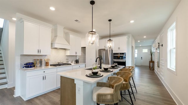 kitchen featuring a sink, appliances with stainless steel finishes, backsplash, light countertops, and a kitchen island with sink