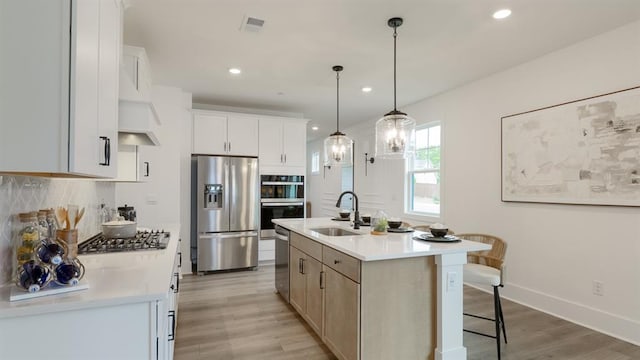 kitchen with appliances with stainless steel finishes, a sink, backsplash, light countertops, and light wood-style flooring