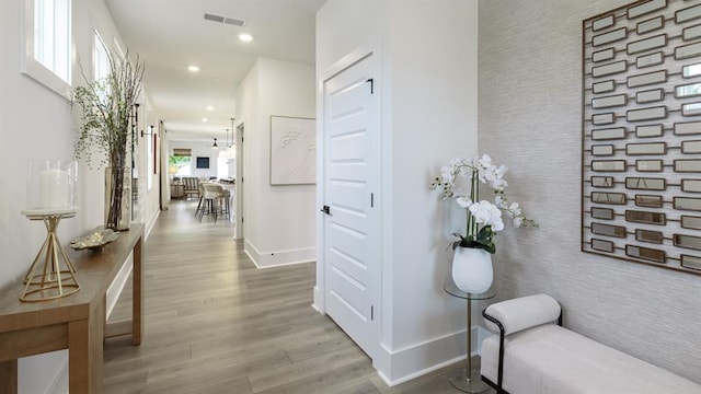 hall featuring an accent wall, baseboards, wood finished floors, recessed lighting, and wallpapered walls