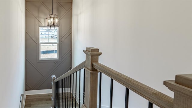 stairs with a chandelier, a decorative wall, and wood finished floors