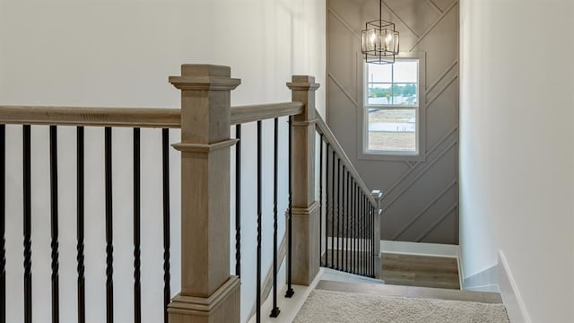 stairway featuring a chandelier, a decorative wall, wood finished floors, and baseboards