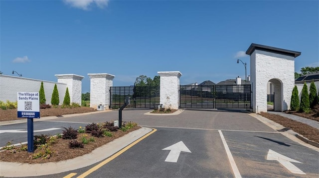 view of asphalt street featuring a gate, curbs, and street lighting